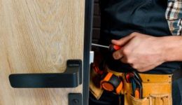 Ilustracja przedstawia profesjonalistę montującego drzwi wejściowe i klamkę NEWAY